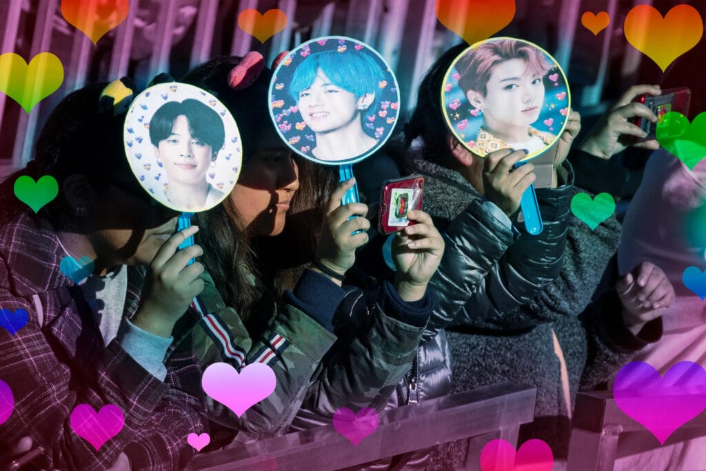 Three people holding fans with images of Jimin, V, and Jungkook from BTS.